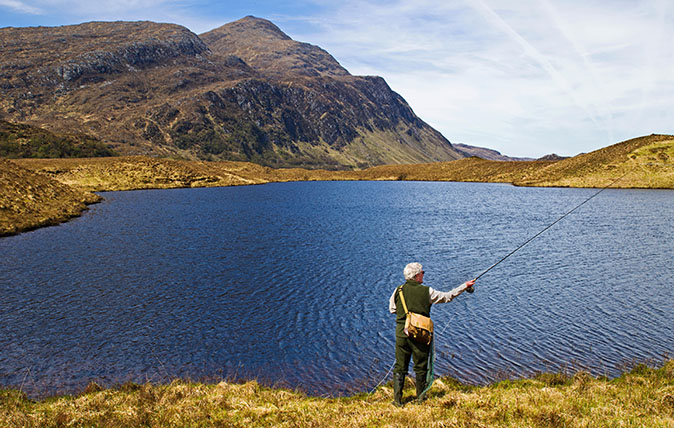 Angler fly-fishing for wild brown trout on hill loch on Reay Forest Estate, Sutherland, Ben Stack in the background, Scottish Highlands, Scotland, UK